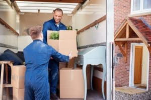 Des travailleurs de l'entreprise de déménagement déchargent des meubles et des boîtes du camion dans une nouvelle maison le jour du déménagement